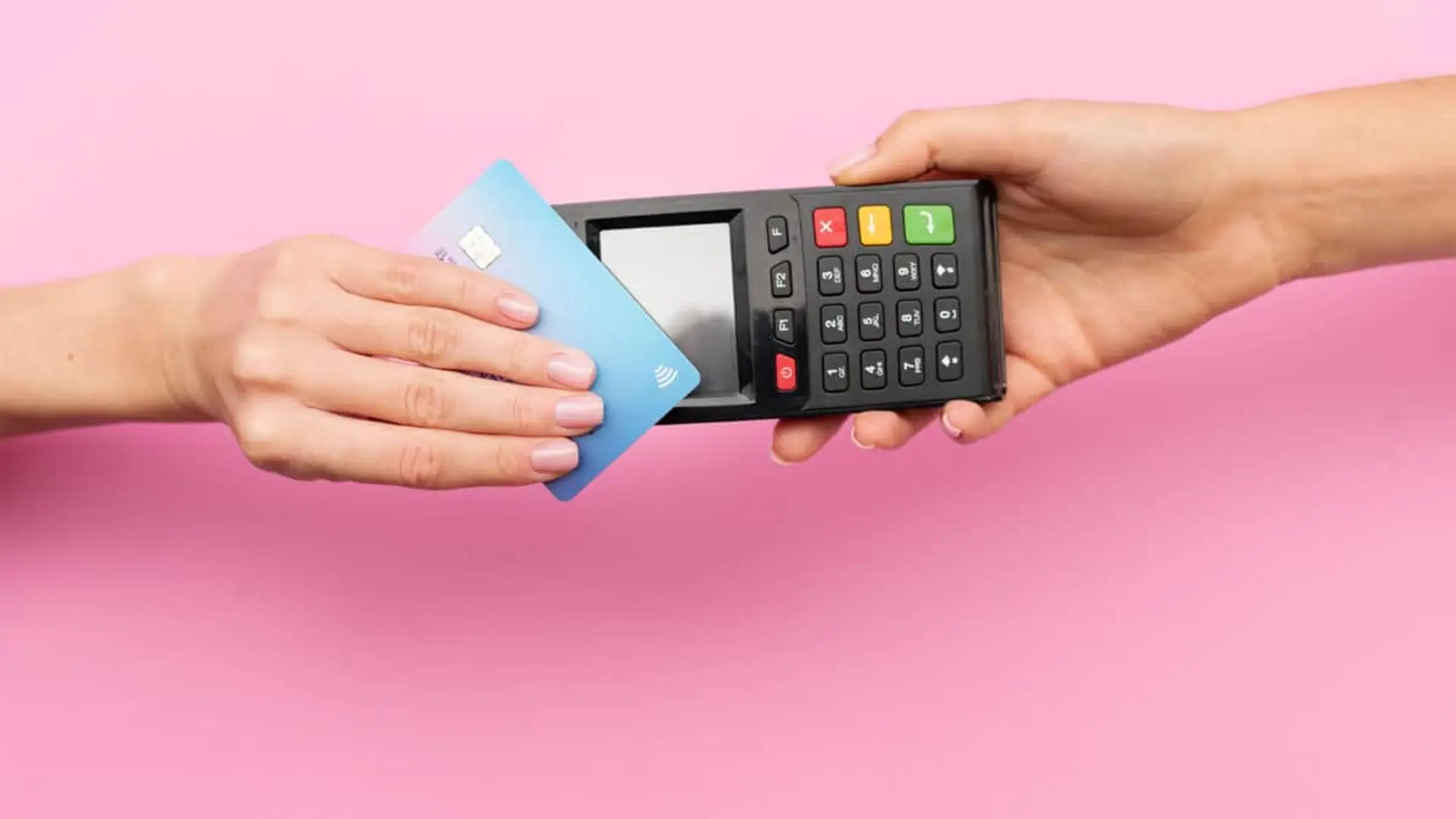 Pagar con tarjeta podría estar arruinando tu ahorro sin que te des cuenta Primer plano de pago contactless con tarjeta de crédito azul en datáfono sobre fondo rosa.