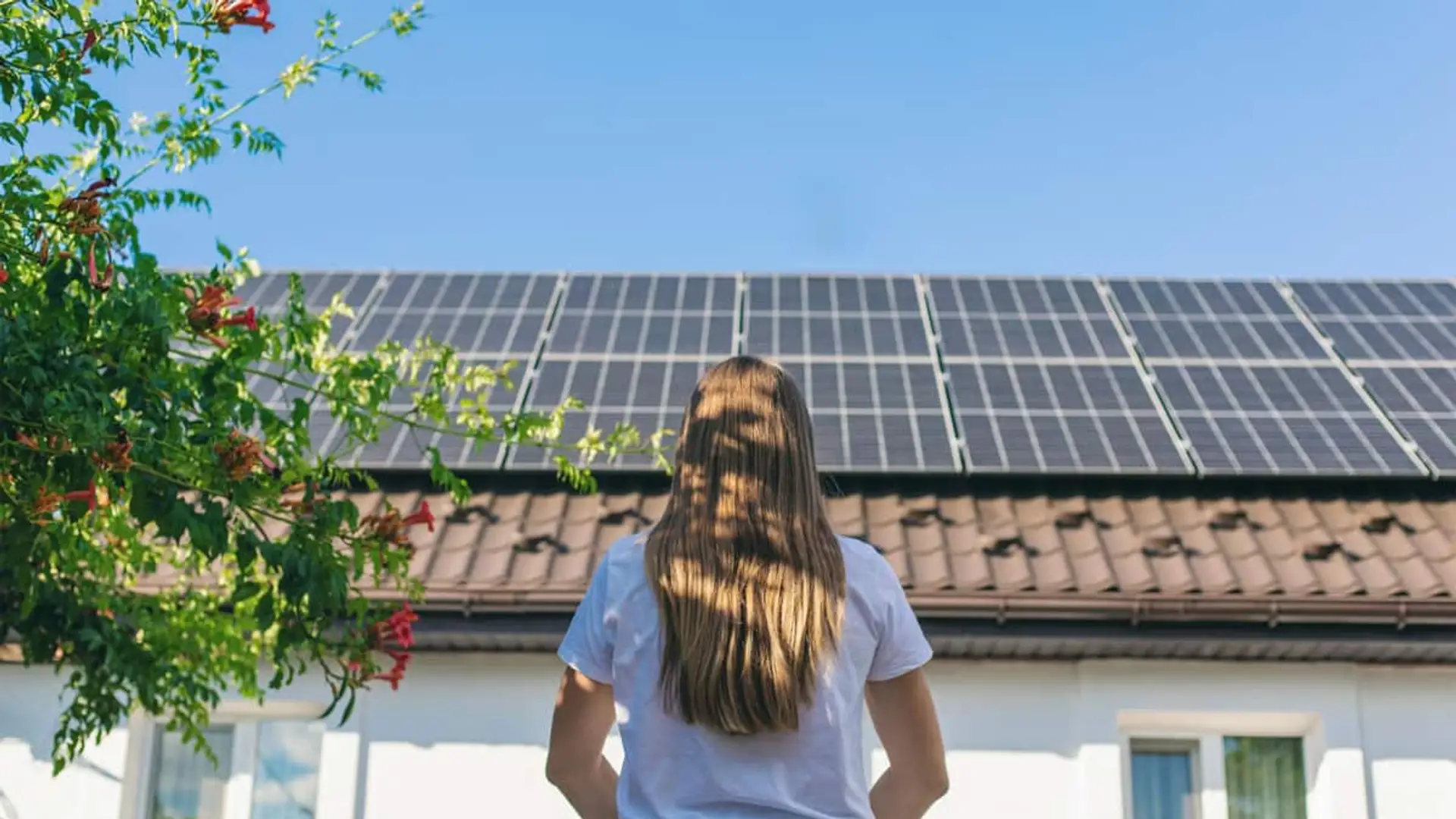 Mujer observando paneles solares instalados en el tejado de una vivienda unifamiliar.