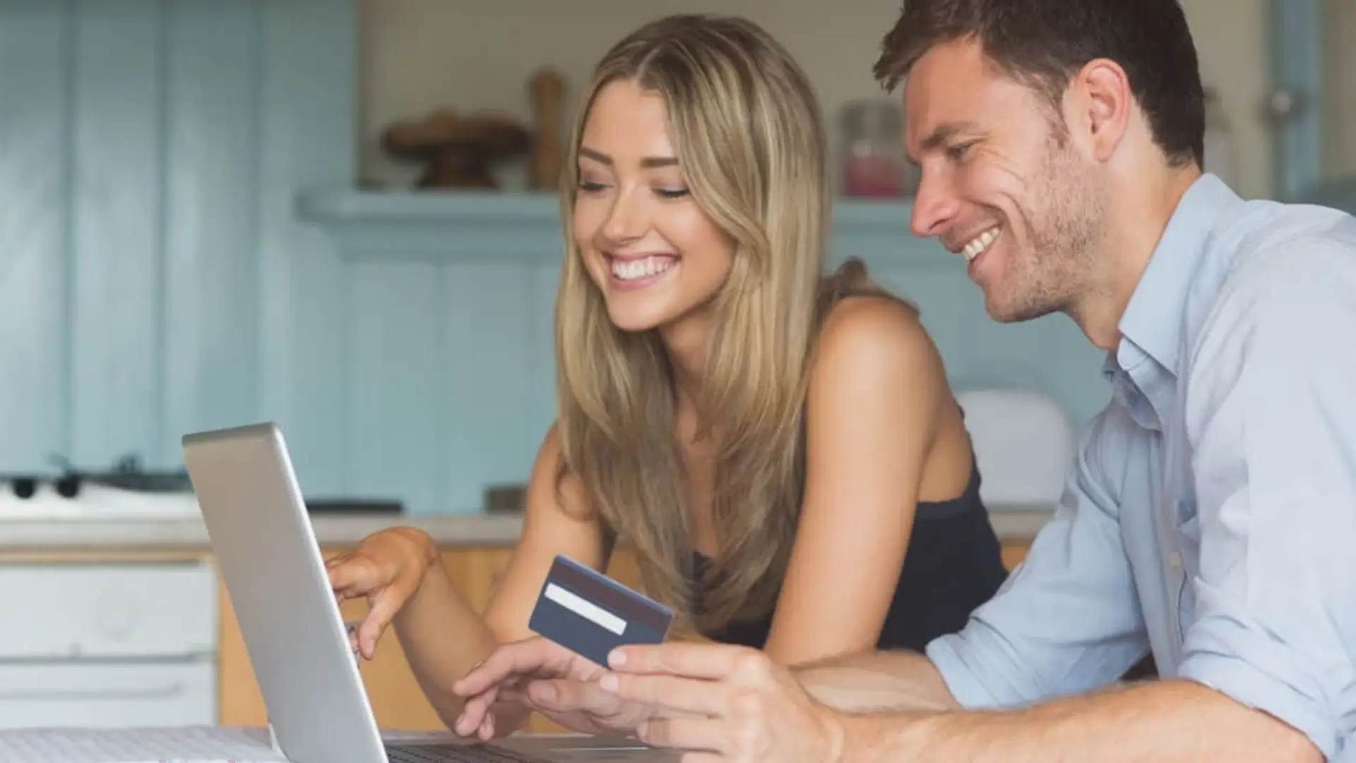 Pareja joven usando su tarjeta bancaria frente a un portátil para contratar productos financieros.