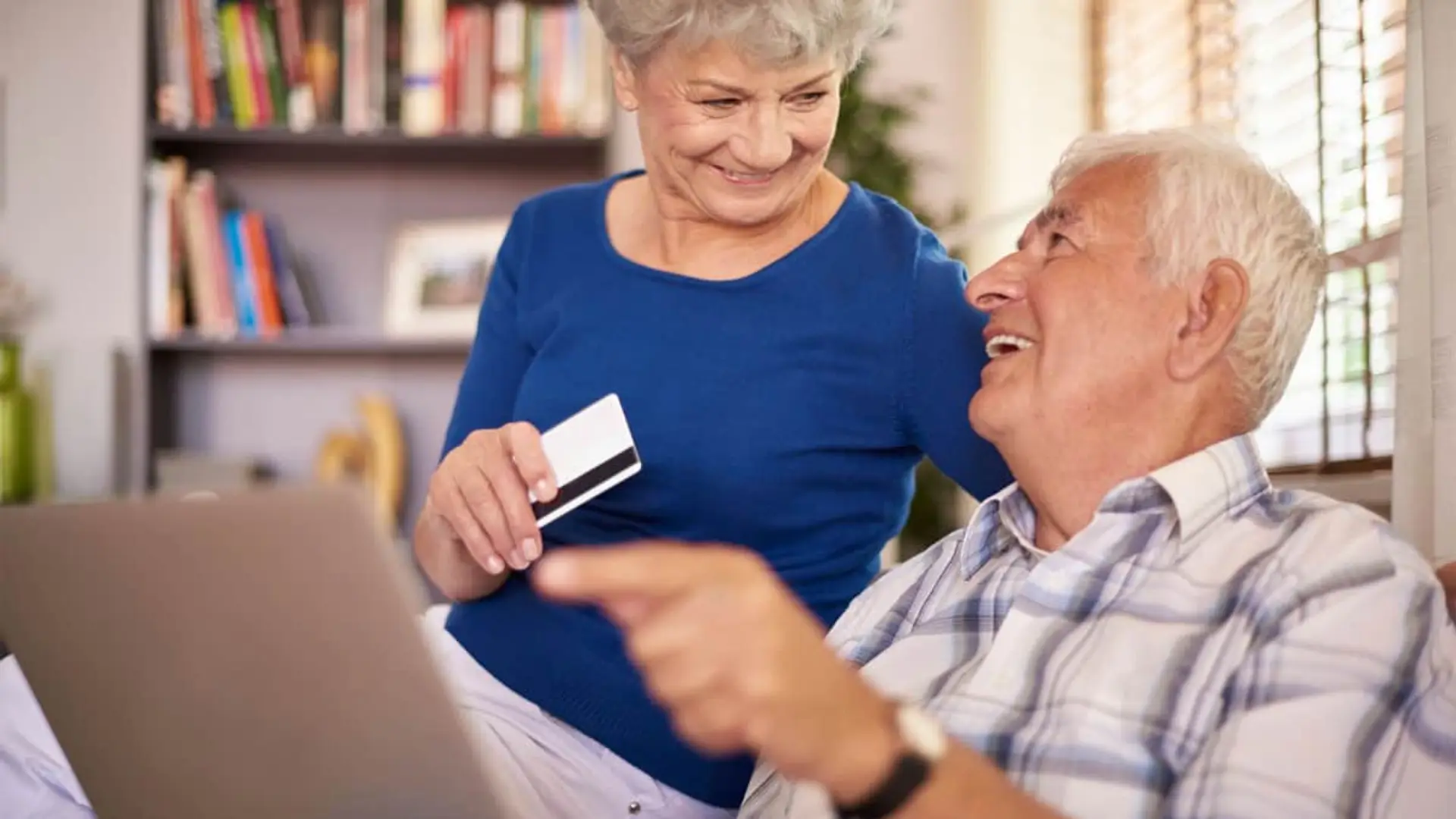 Cuándo se cobra la pensión en noviembre de 2025: Unicaja y Bankinter se adelantan a BBVA, CaixaBank y Santander Pareja de jubilados realizando compra online segura con tarjeta de crédito y ordenador portátil.