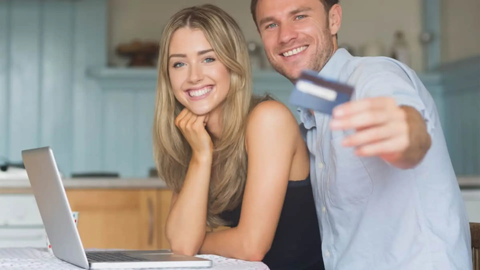 Pareja sonriente con tarjeta y portátil aprovechando promociones bancarias y bonificaciones por abrir una cuenta online.