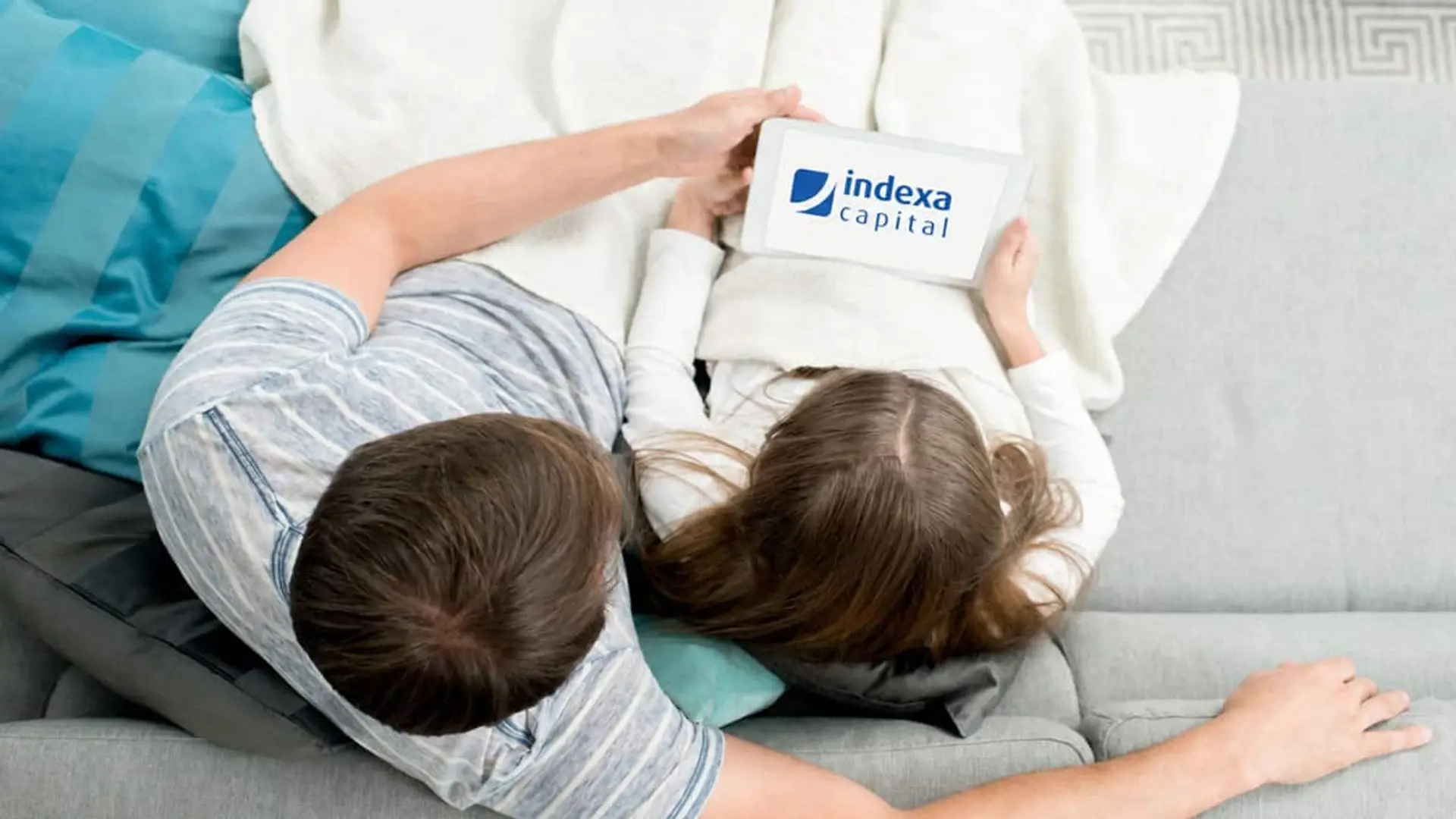Persona adulta y menor sentadas en un sofá viendo una tablet con el logotipo de Indexa Capital en pantalla