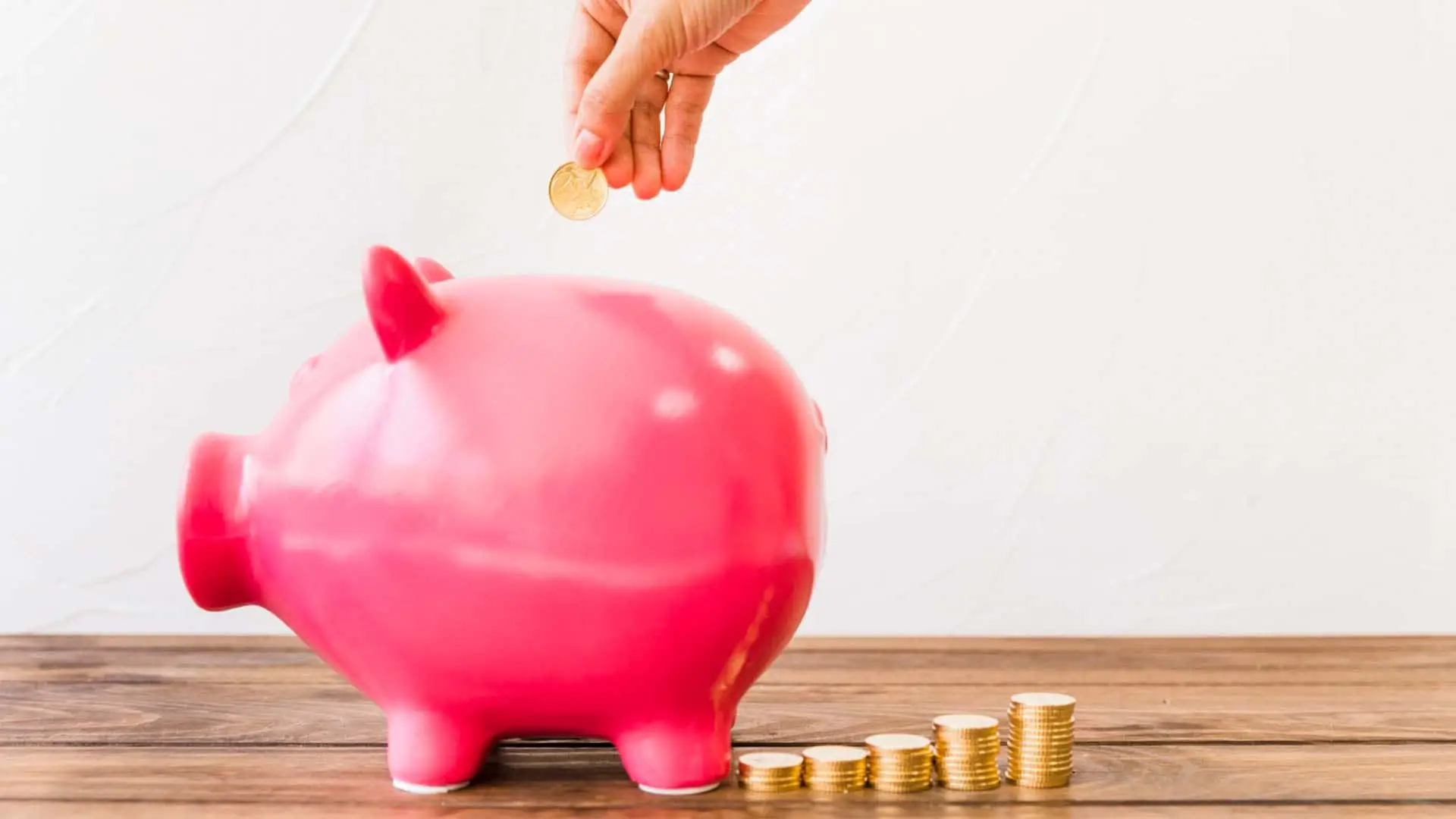Mano introduciendo una moneda en una hucha de cerdito, simbolizando el ahorro y la rentabilidad de los depósitos.