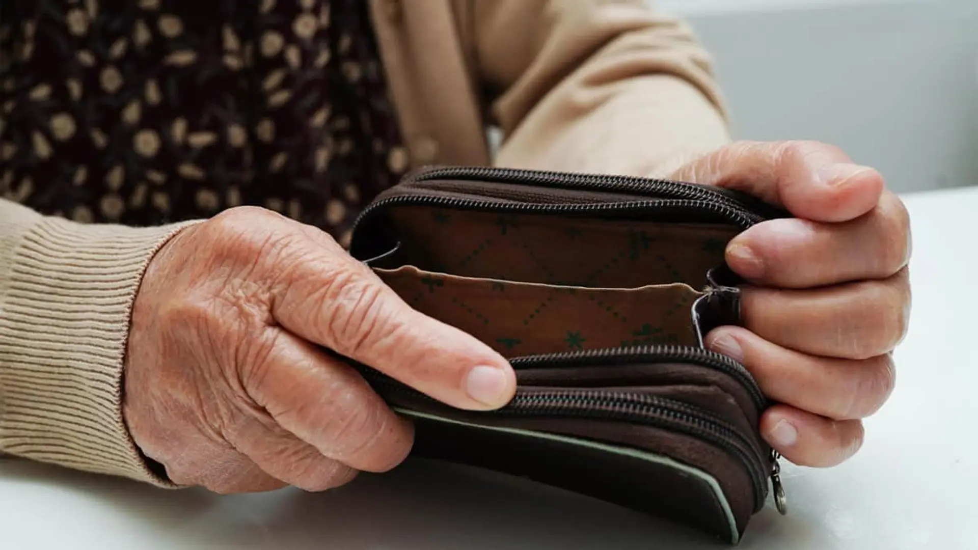 Manos de una persona mayor sujetando una cartera vacía, representando la espera de cobro de pensión.