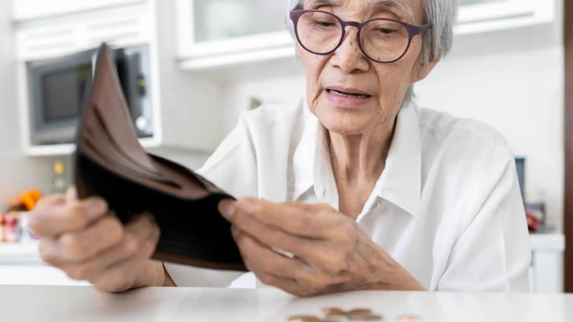 Mujer mayor mirando una cartera vacía con preocupación, reflejando problemas de ahorro o bajas pensiones.