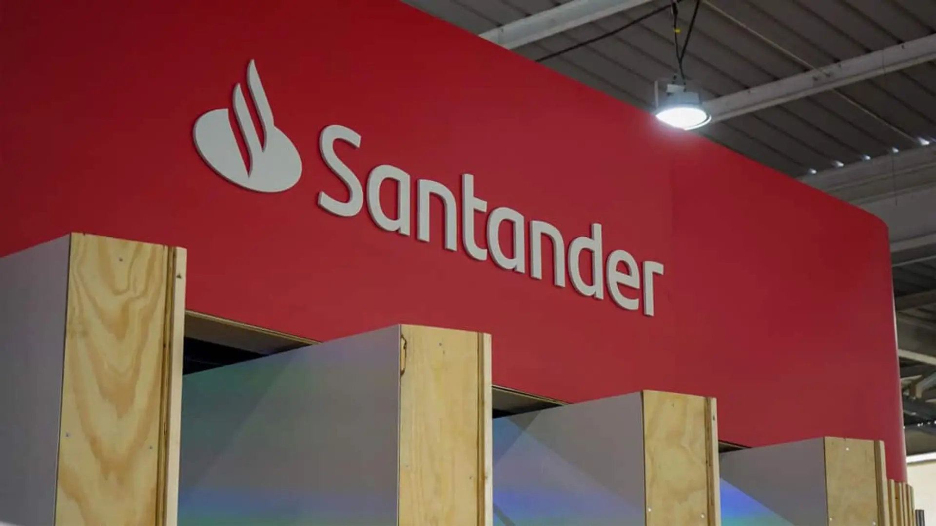 Rótulo del Banco Santander en un stand interior con fondo rojo.