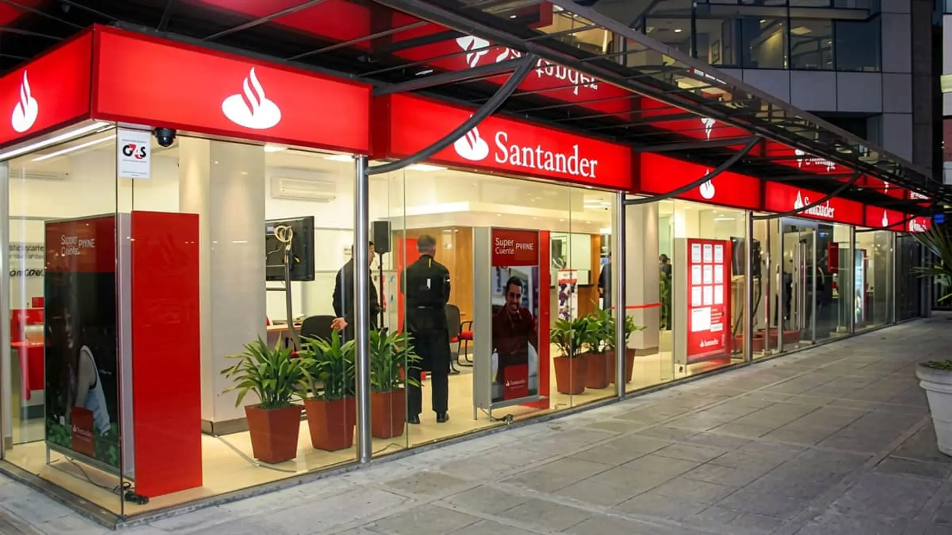 Fachada exterior de una oficina de Banco Santander con grandes cristaleras y carteles rojos corporativos.