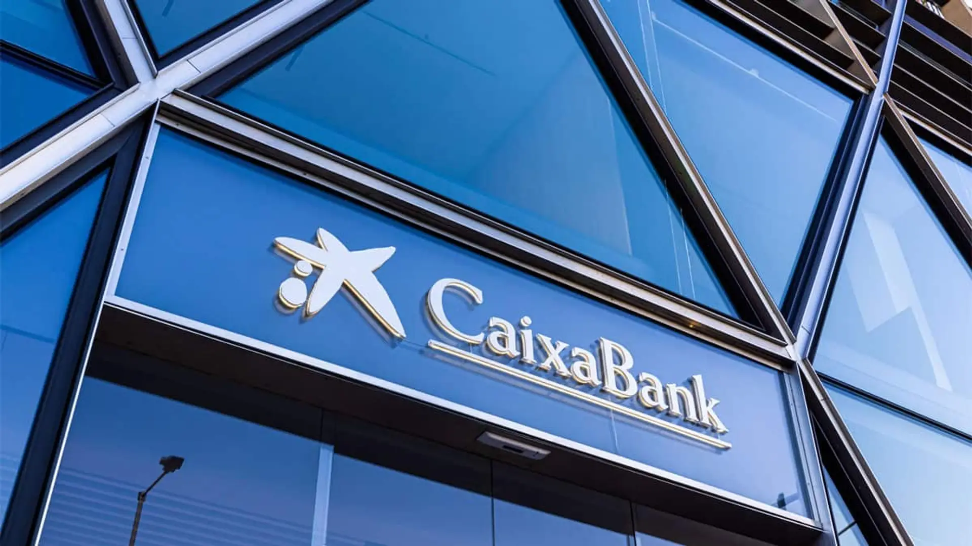 Entrada de una sucursal de CaixaBank con fachada acristalada y el nombre del banco en la parte superior.