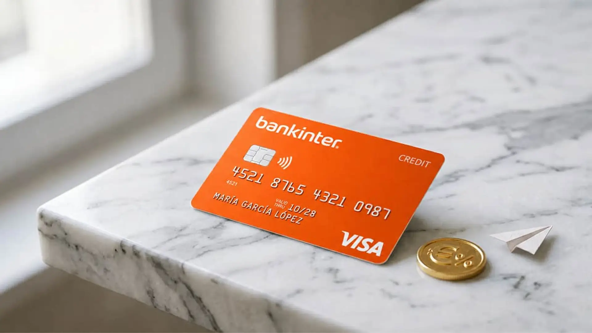 Tarjeta de crédito Bankinter sobre mesa de mármol con moneda y avión de papel