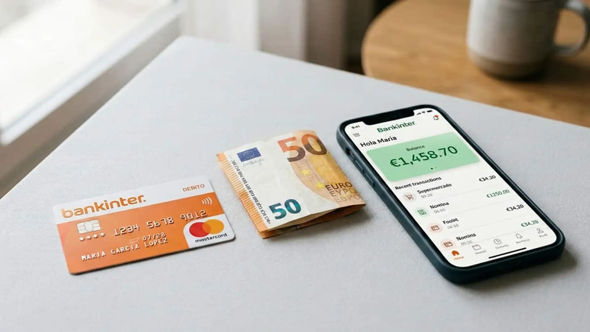 Tarjeta de Bankinter, un billete de 50 euros y un móvil con la app bancaria sobre una mesa