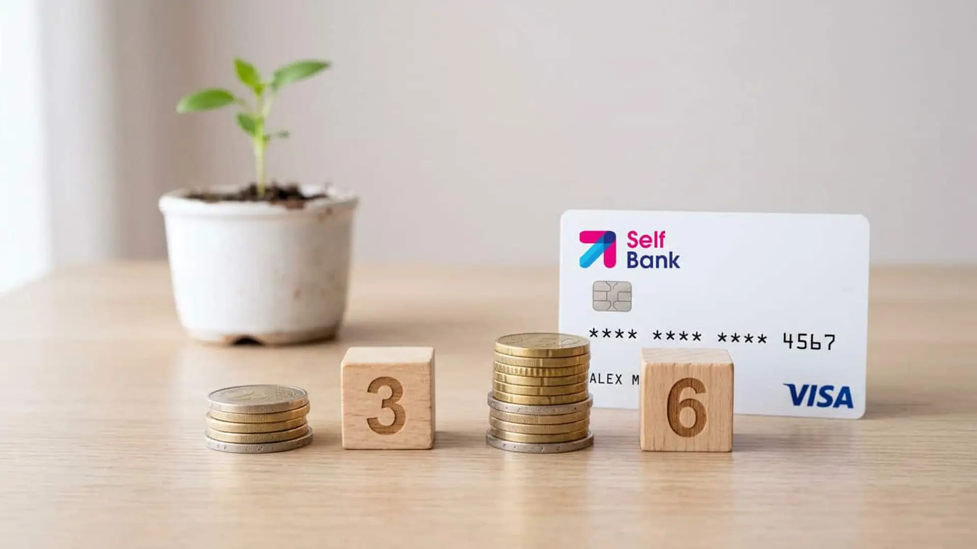 Tarjeta Visa de Self Bank junto a varias pilas de monedas y bloques de madera con los números 3 y 6 sobre una mesa.