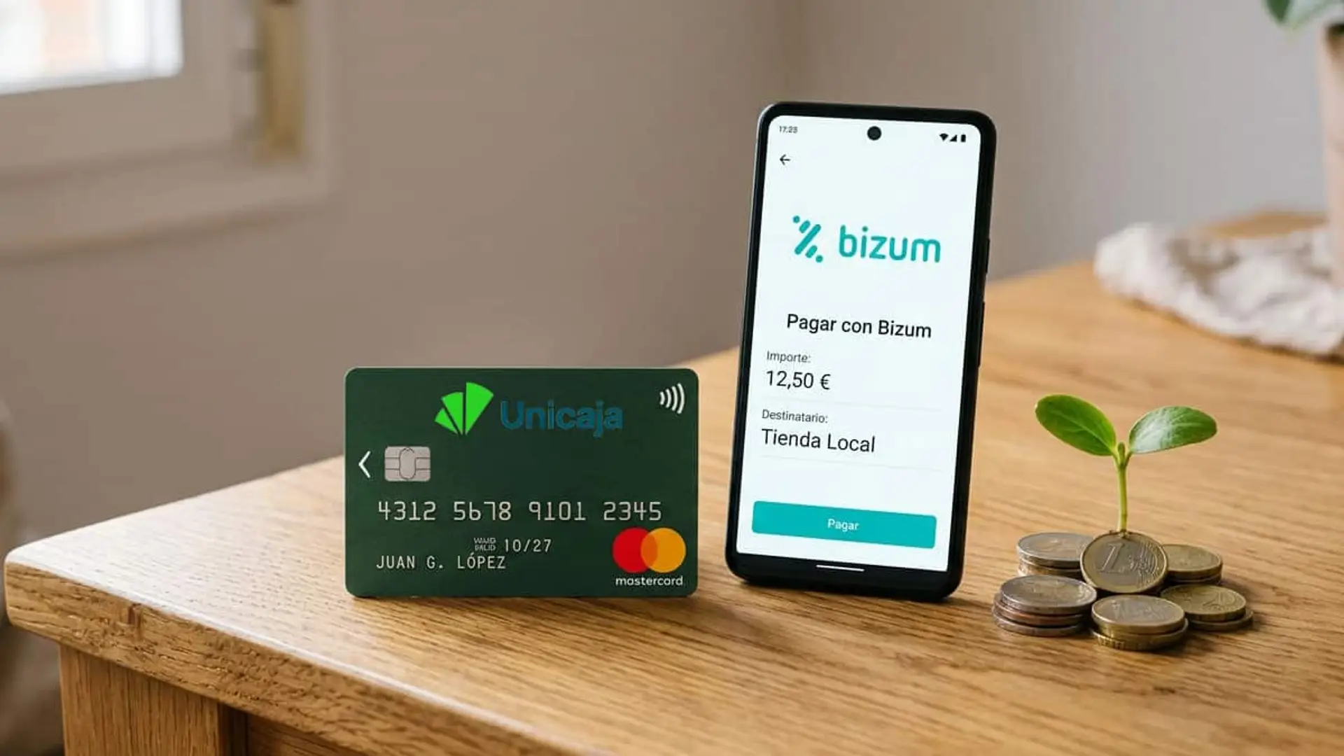 Tarjeta de Unicaja junto a un móvil con una pantalla de pago con Bizum y varias monedas de euro