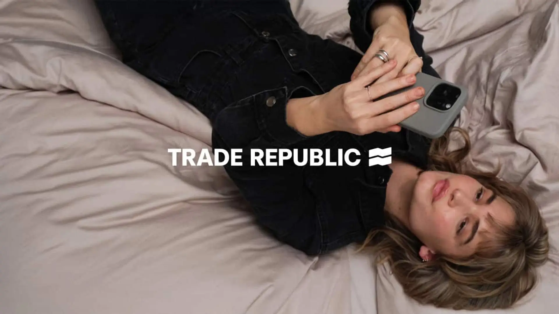 Trade Republic celebra la Navidad: así puedes conseguir 300€ en acciones por tiempo limitado Mujer tumbada en la cama usando la aplicación de Trade Republic en su teléfono móvil.
