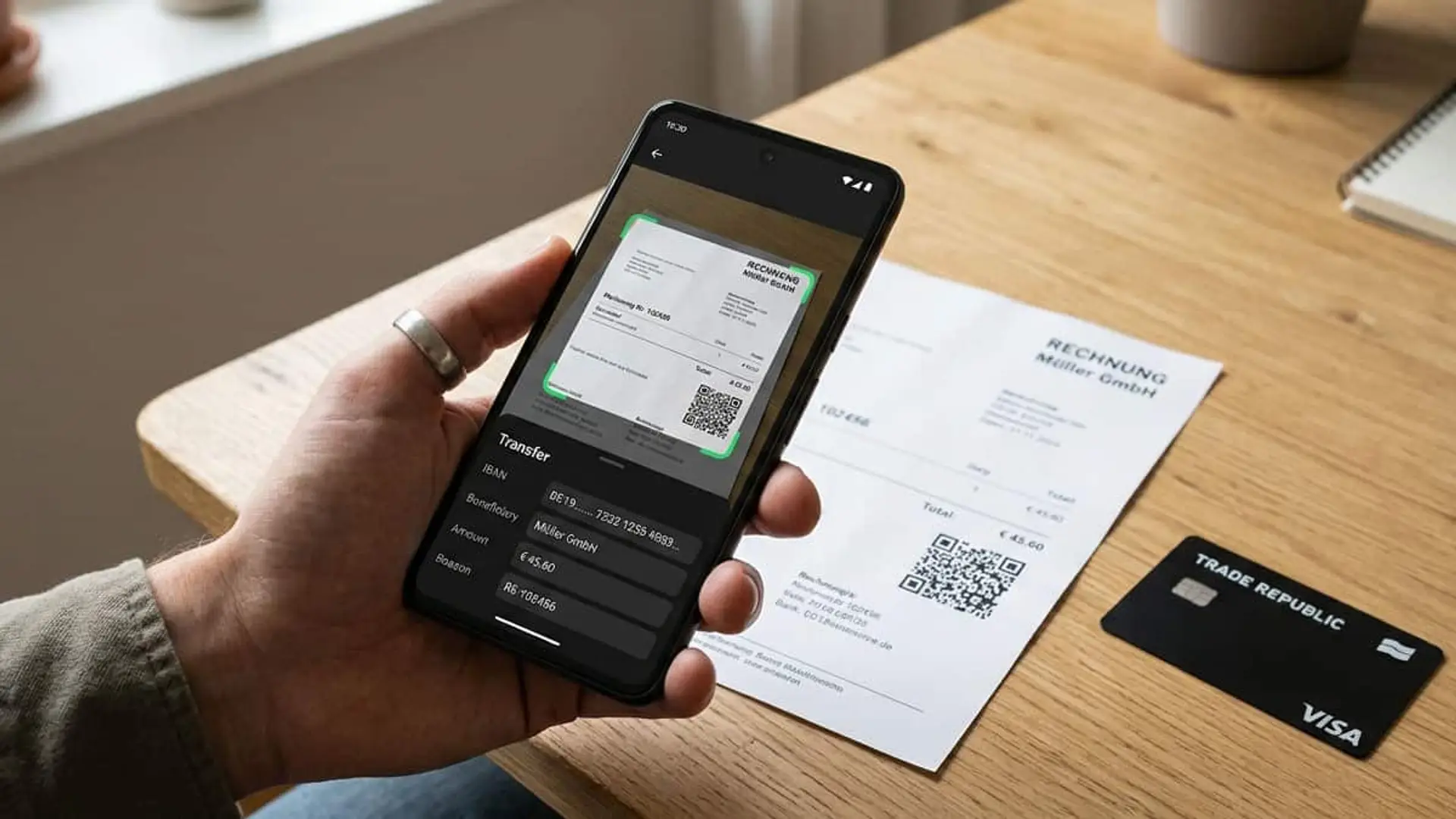 Persona escaneando una factura con un móvil para realizar una transferencia, junto a una tarjeta Visa de Trade Republic.