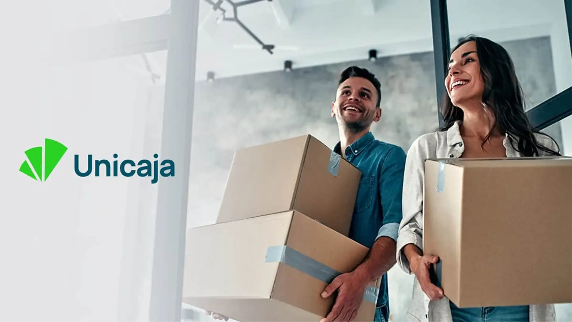 Pareja cargando cajas de mudanza junto al logo de Unicaja, representando la compra de vivienda o una hipoteca.