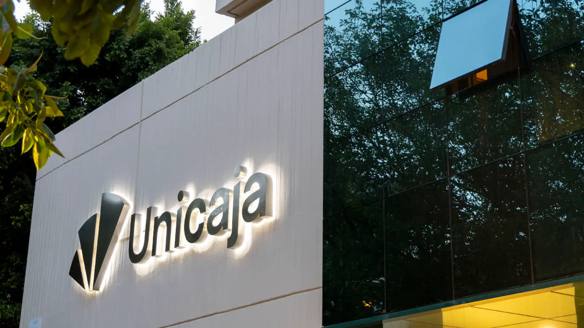 Unicaja quiere crecer en crédito al consumo y WiZink encaja en sus planes: por qué la operación no está cerrada Fachada exterior de un edificio de Unicaja Banco con el logotipo corporativo iluminado sobre la pared.