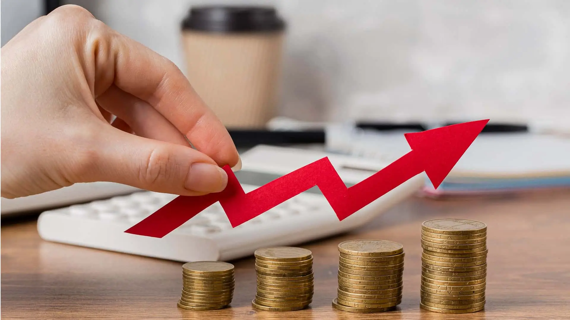 Concepto de crecimiento financiero: mano coloca flecha ascendente sobre pilas de monedas. Inversión y rentabilidad económica.
