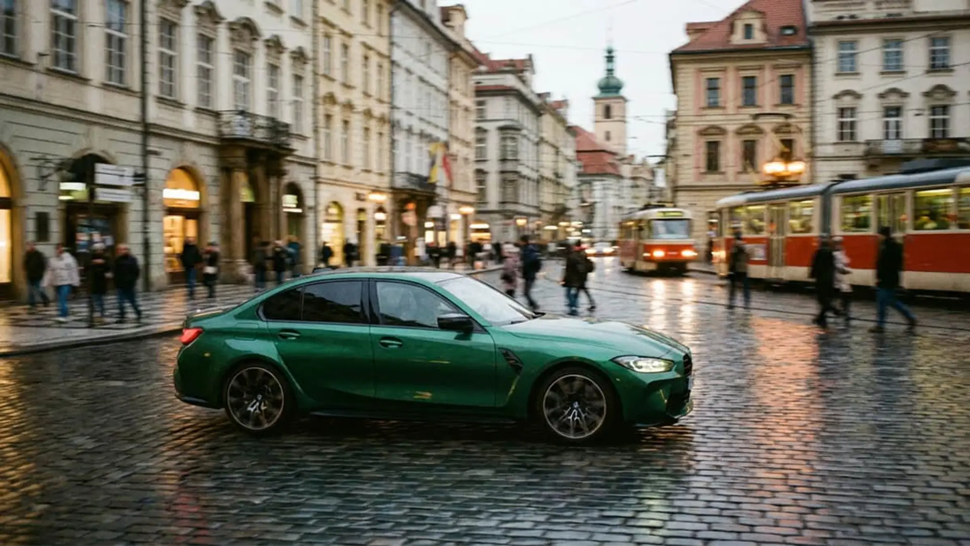 Coche BMW verde circulando por una calle adoquinada de una ciudad con un tranvía al fondo.