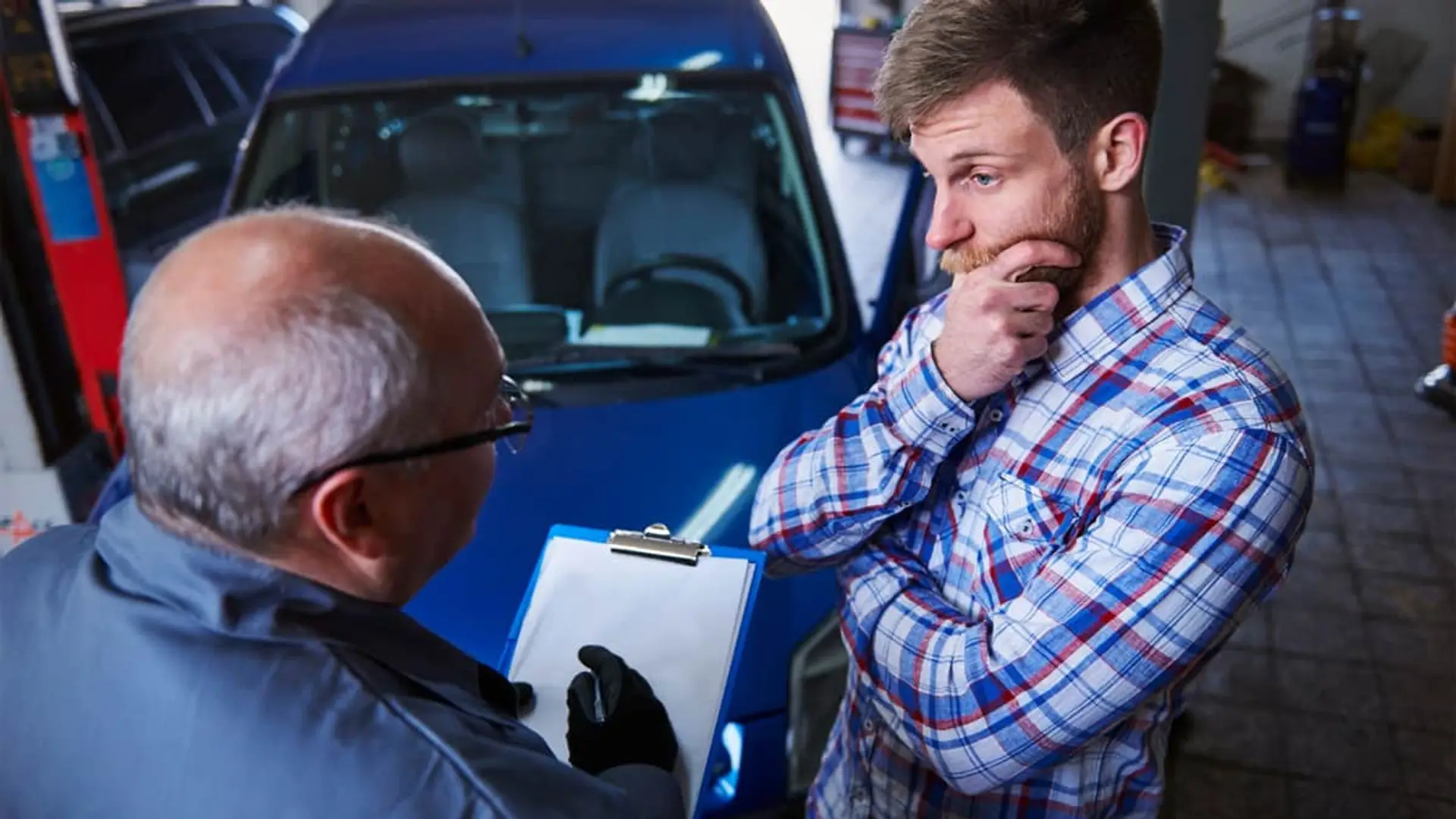 Mecánico asesorando a un cliente en un taller sobre la reparación del coche o la gestión de un parte de seguro.