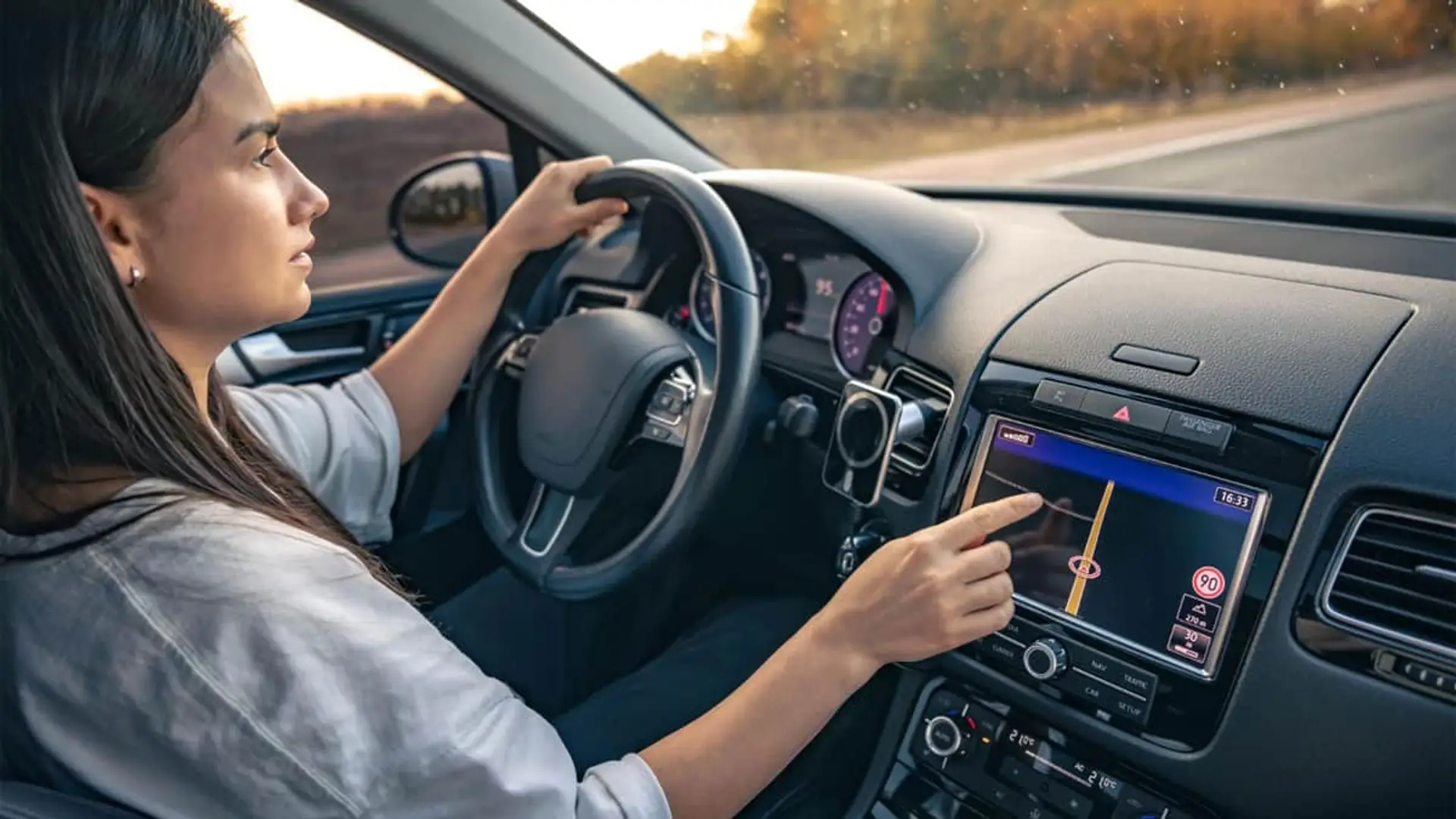 Tu coche también se puede hackear: así se están adaptando las aseguradoras Mujer conduciendo un vehículo y usando la pantalla de navegación GPS para representar el uso de tecnología en el coche.