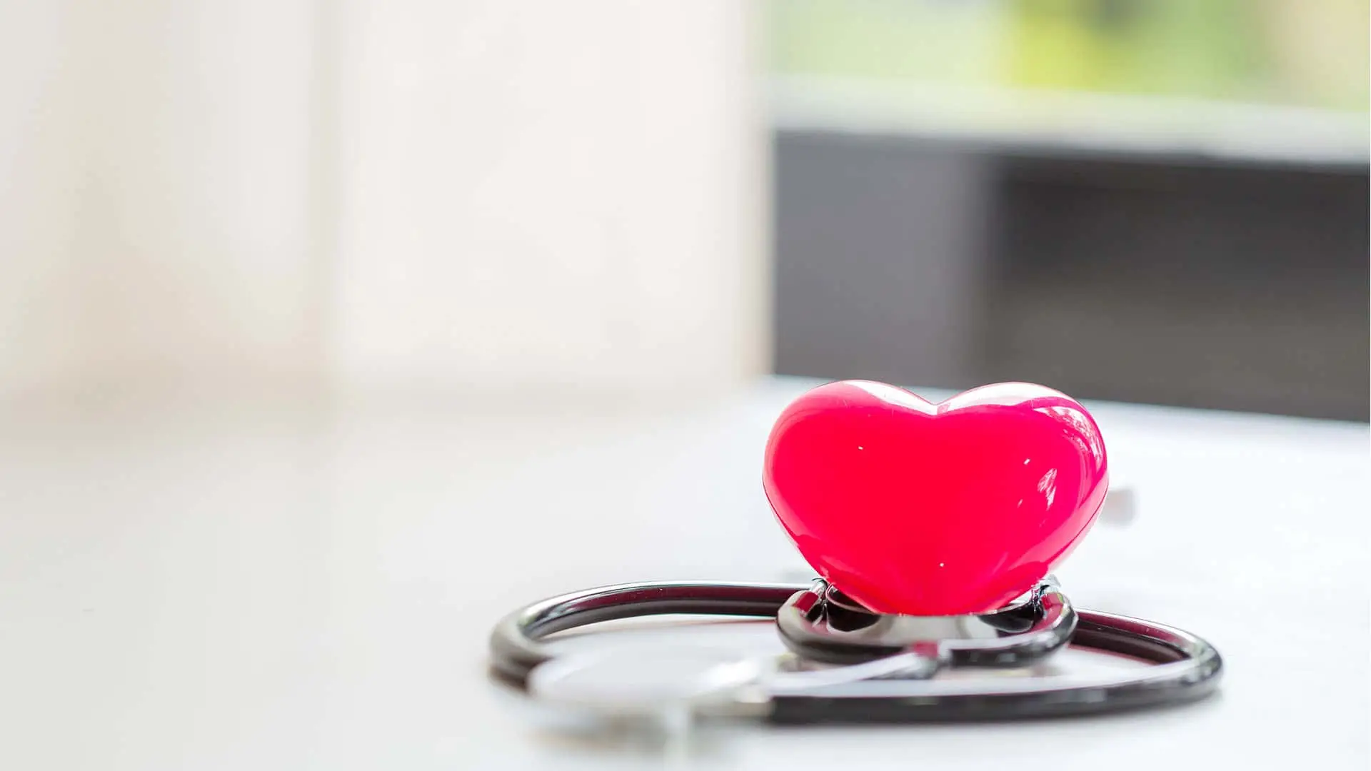 Corazón rojo de plástico sobre un estetoscopio en una mesa blanca.