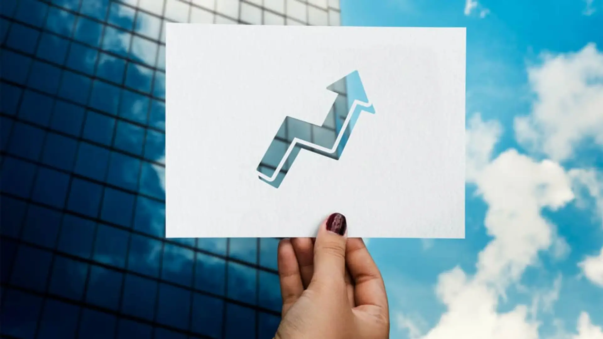 Las aseguradoras extranjeras baten récords en España: 1000 millones en dividendos y un crecimiento del 71% Mano sosteniendo una tarjeta con un recorte de flecha hacia arriba, simbolizando crecimiento financiero y éxito empresarial.