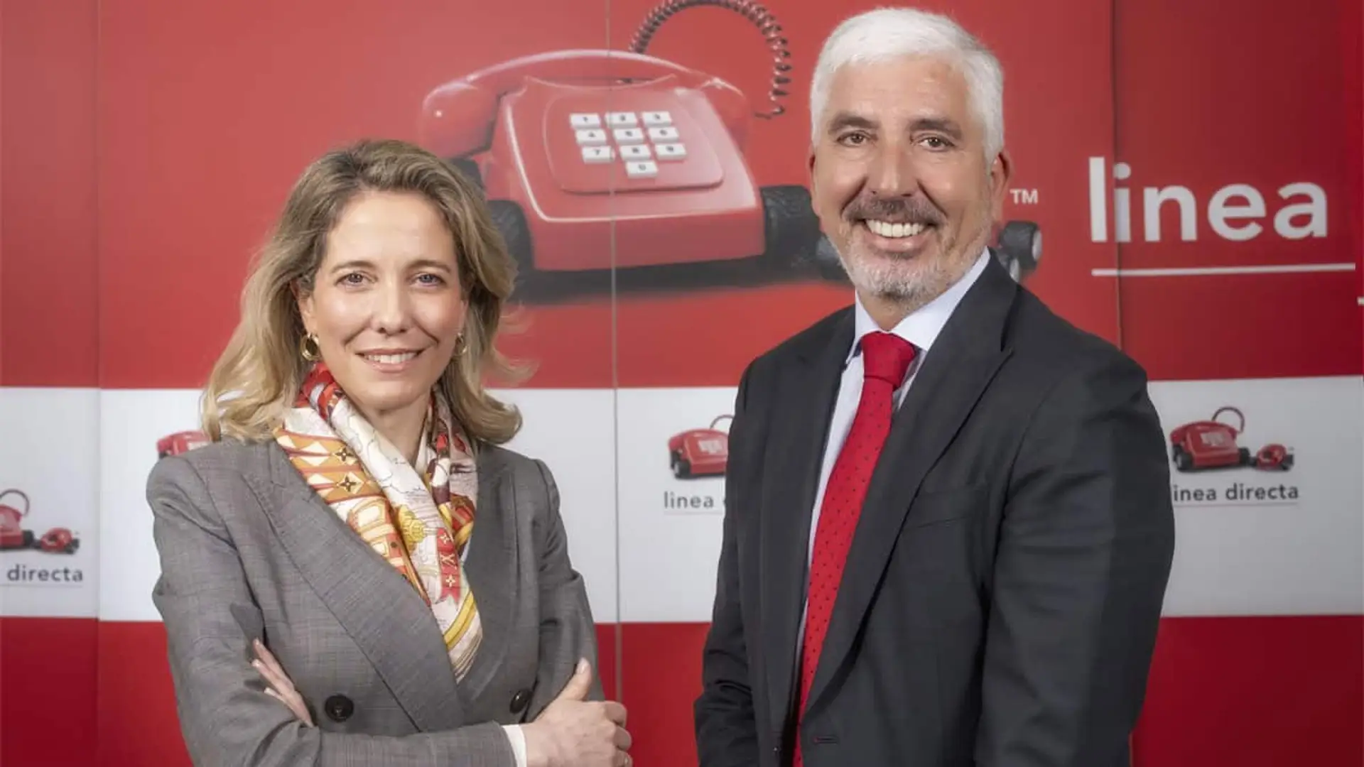 Dos directivos de Línea Directa posando ante un panel corporativo con el logotipo de la empresa