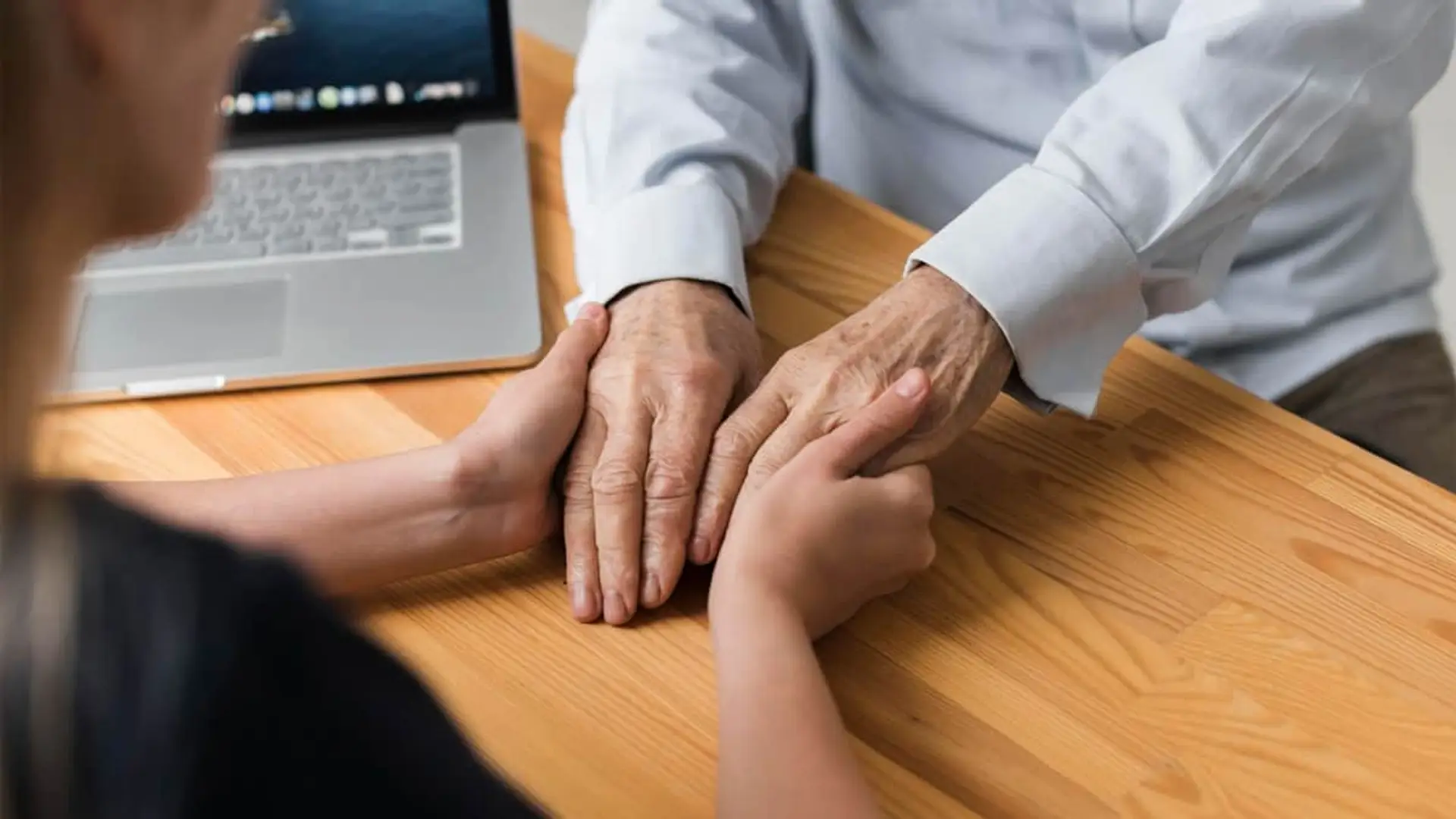 Iris Global mejora su ayuda en la gestión de decesos gracias a la innovación tecnológica Empleado sostiene las manos de un cliente en una reunión de asesoramiento.