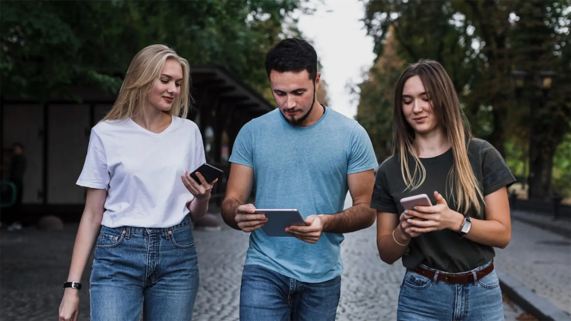 Estos son los seguros que más contratan los jóvenes en España Grupo de jóvenes caminando por la calle mientras usan sus teléfonos móviles y una tablet, conectados a internet.