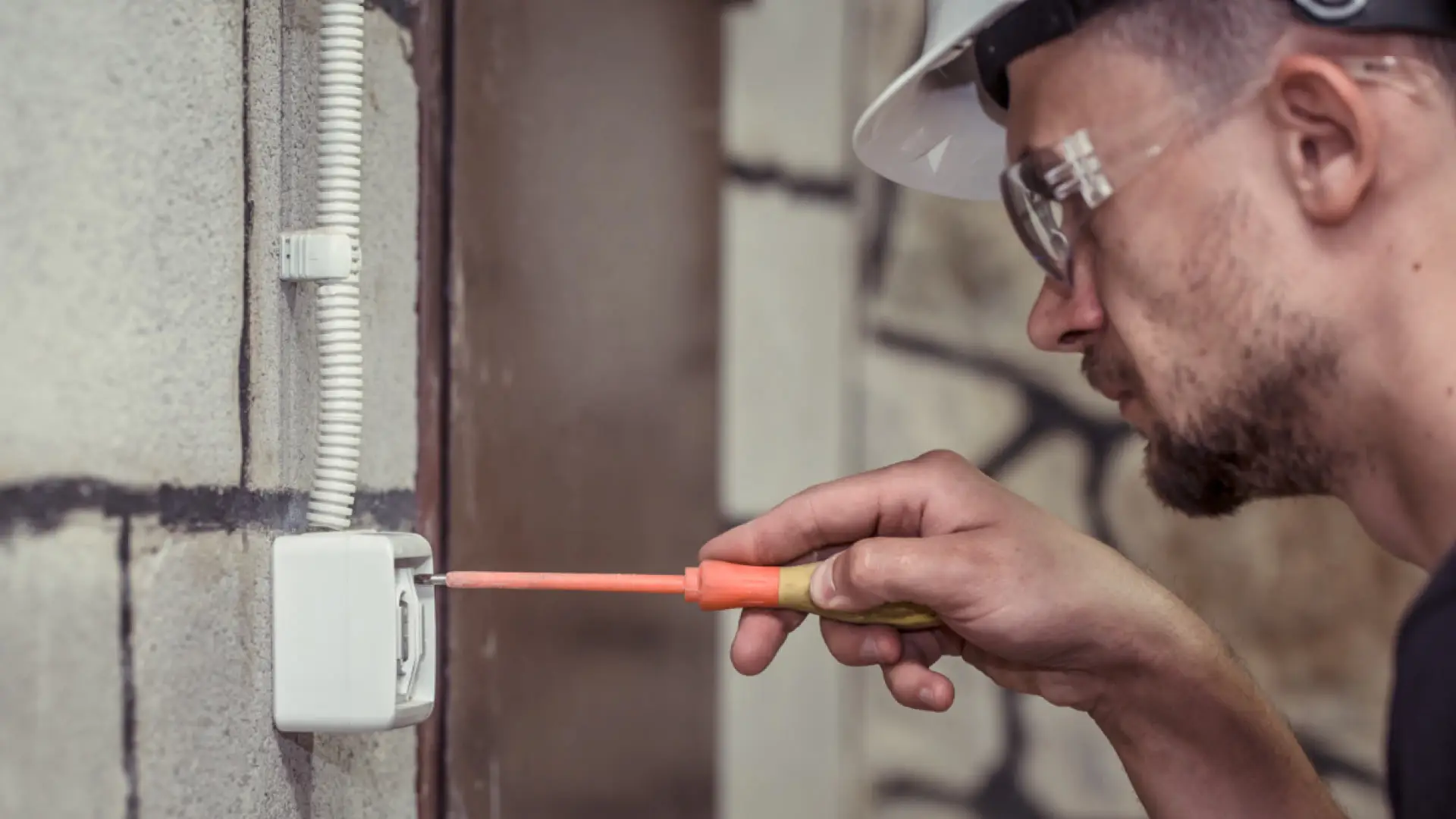 Estos son los siniestros en el hogar que más crecen en verano: así debes proteger tu casa Electricista profesional con casco y gafas de seguridad reparando un enchufe para solucionar daños eléctricos en una vivienda.