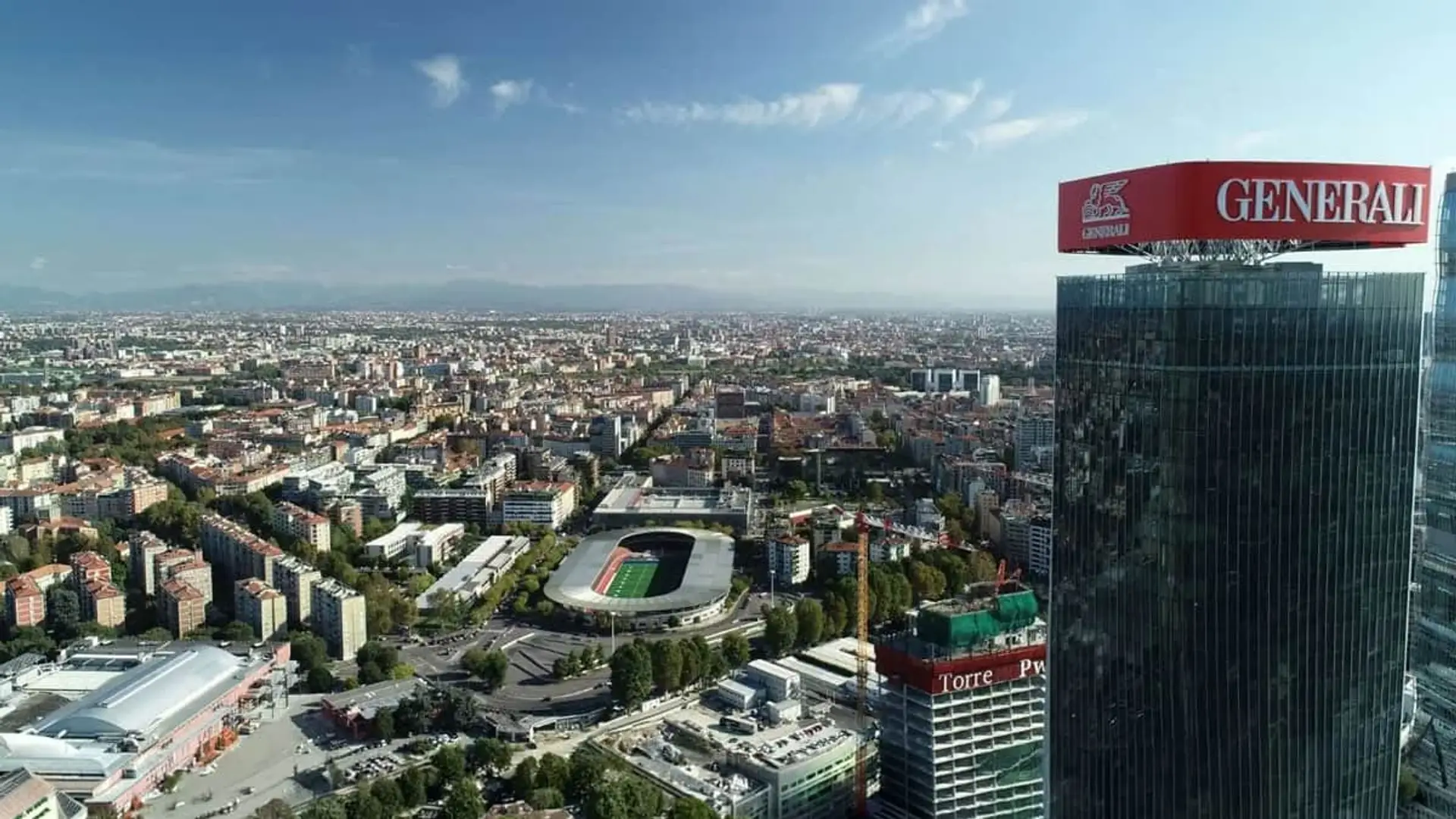 Generali gana menos pero ingresa más por primas: qué significa para tu seguro Torre Generali en Milán: vista aérea del edificio corporativo con el skyline de la ciudad y el estadio de fondo.