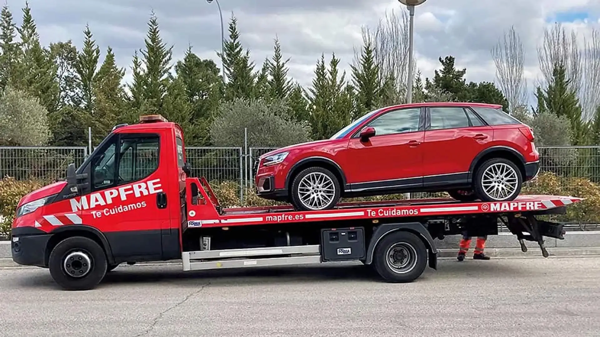 Grúa de Mapfre trasladando un coche rojo como parte del servicio de asistencia en carretera.