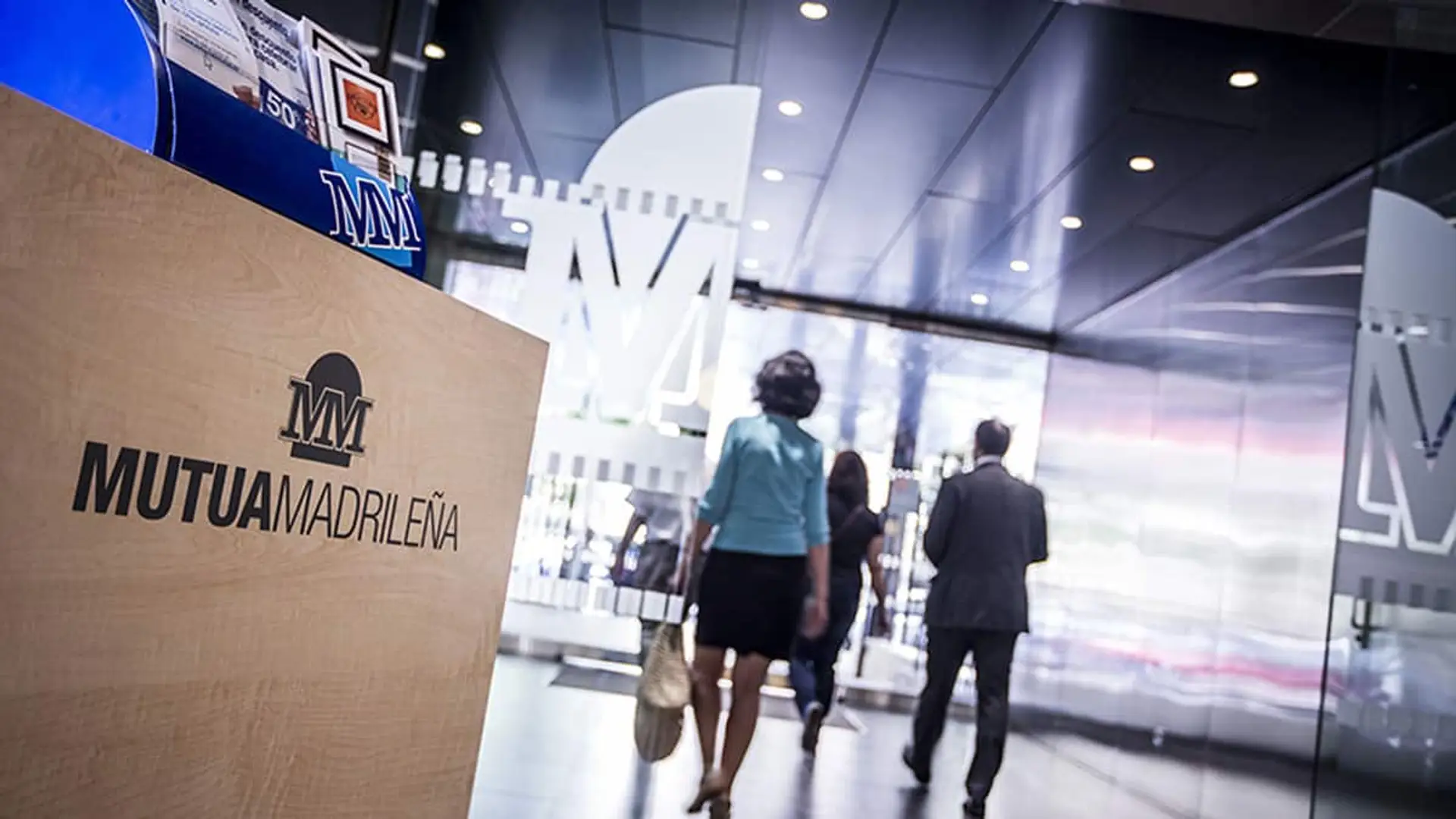 Mutua Madrileña lanza un seguro de accidentes para mayores de 65 años Entrada de la sede de Mutua Madrileña con personas caminando hacia el interior del edificio.