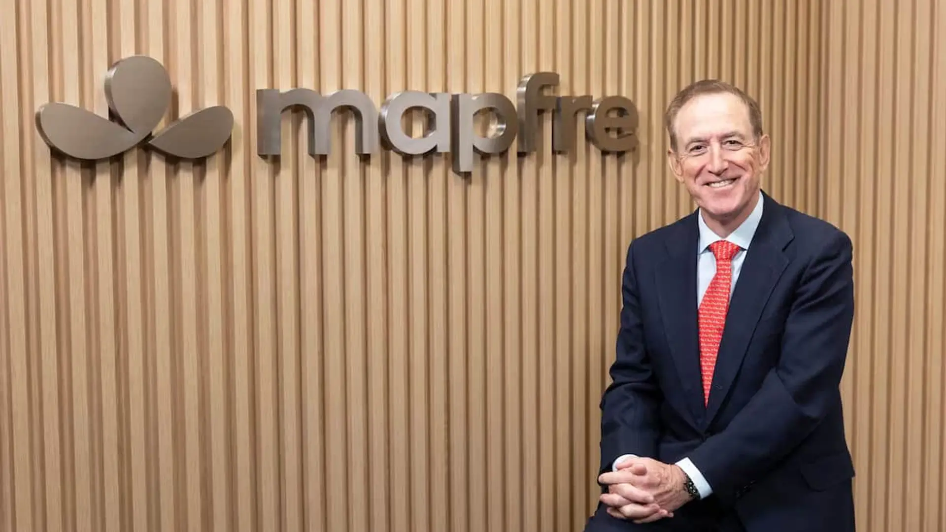 Antonio Huertas, presidente de Mapfre, posando ante el logotipo de la aseguradora sobre una pared de madera.