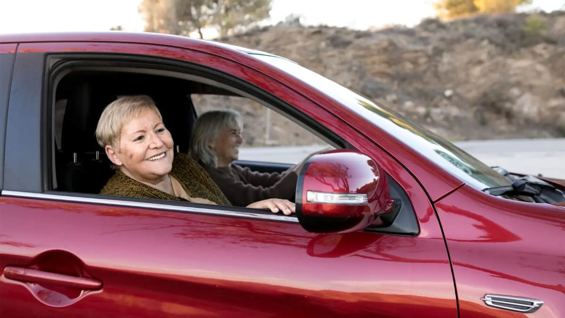Volantazo en el seguro de coche: el triple de conductoras sénior y la mitad de jóvenes Dos mujeres mayores sonrientes disfrutando de un viaje por carretera en un coche rojo.