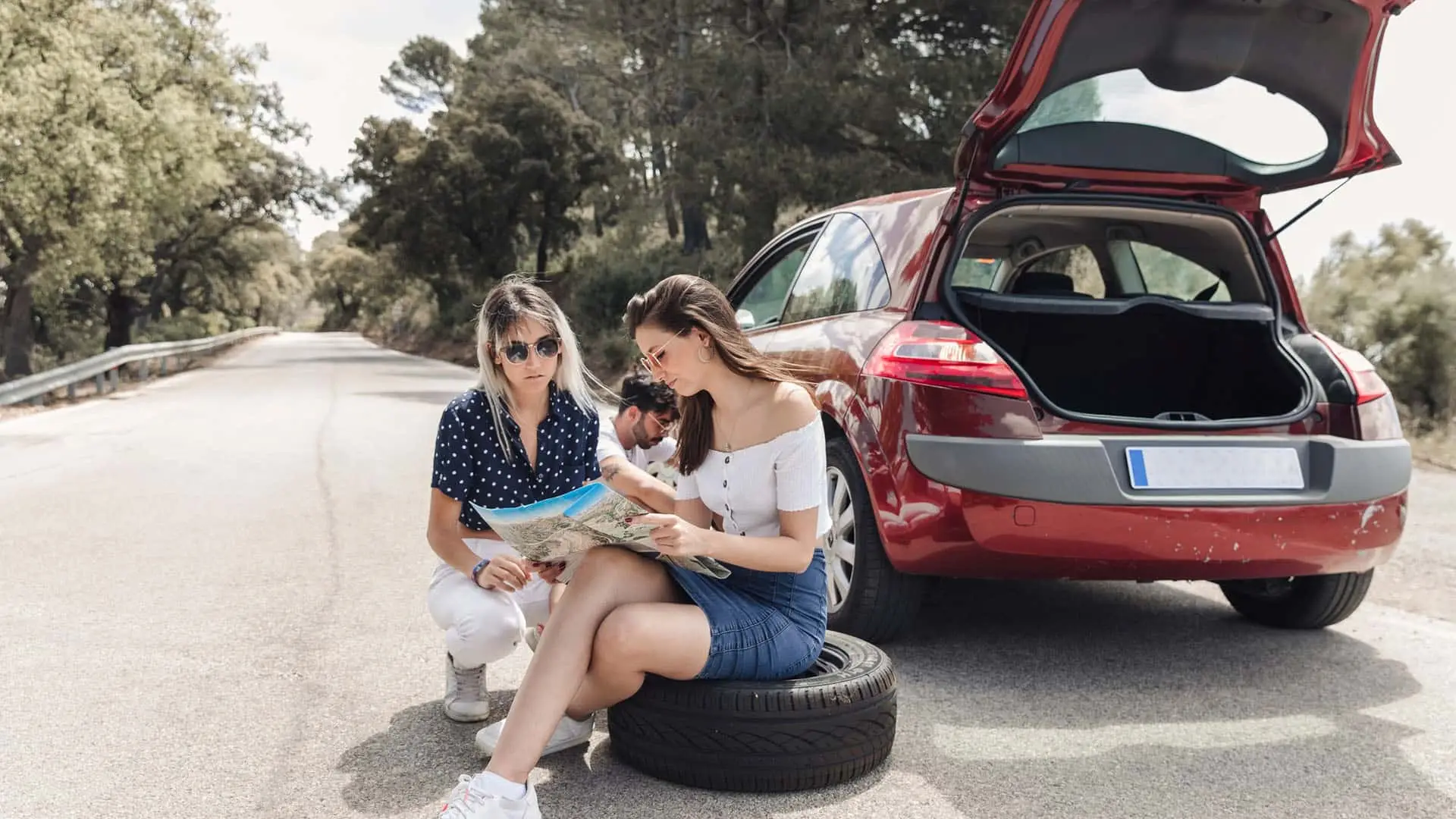 Dos mujeres revisando un mapa junto a un coche averiado en carretera.