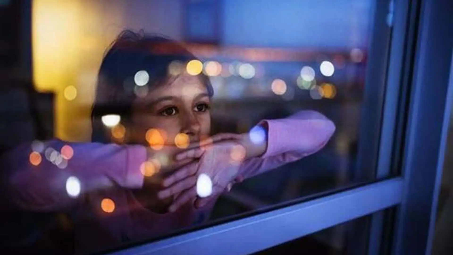 Niña con expresión pensativa mira por la ventana de noche. Concepto de soledad, salud mental infantil y la espera o el anhelo.