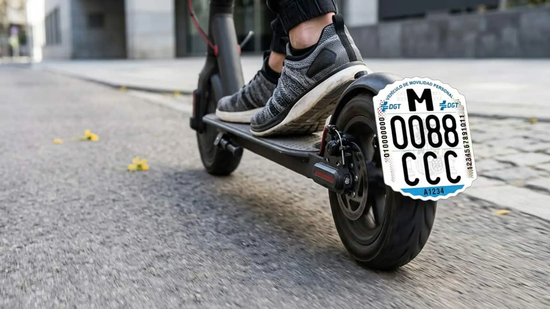 Patinete eléctrico circulando por una calle con una placa identificativa de la DGT sobre la rueda trasera