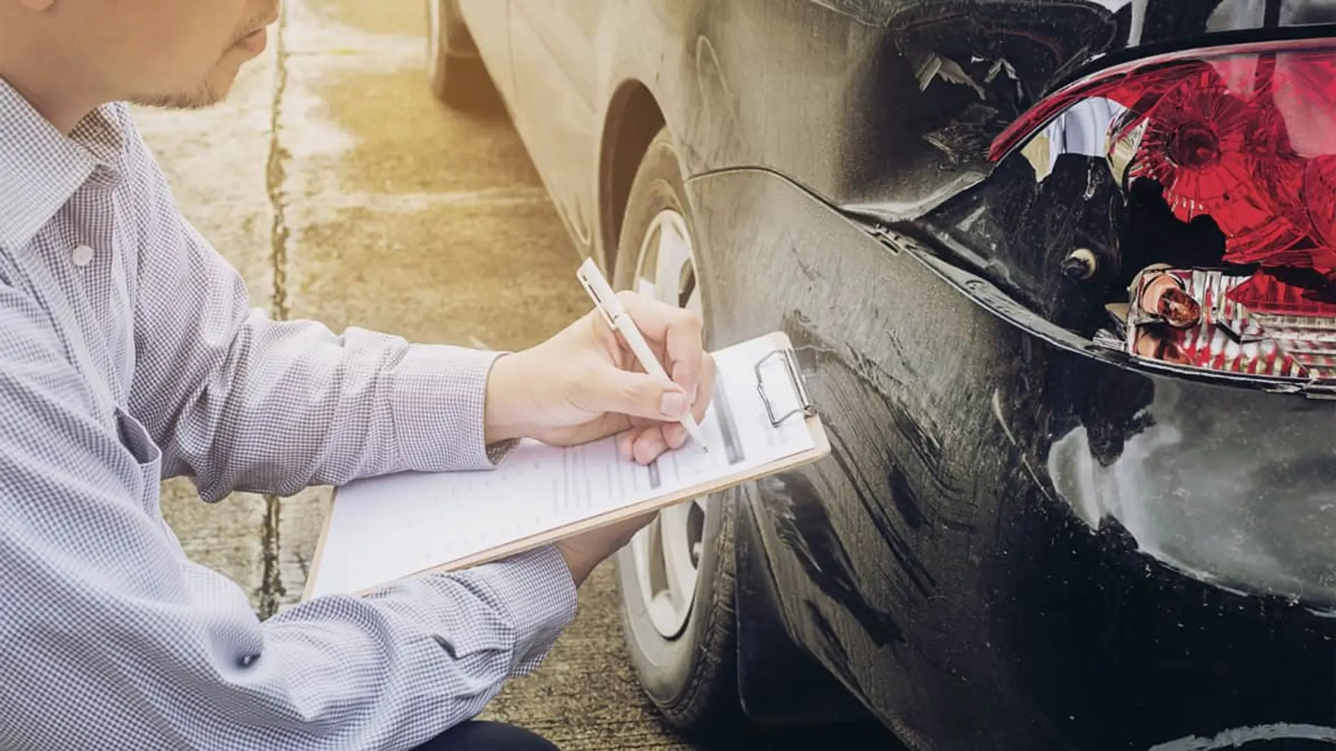 El precio de los seguros de coche subirá en 2026: “No tenemos margen” Conductor rellenando parte amistoso de accidente frente a faro trasero de coche roto.