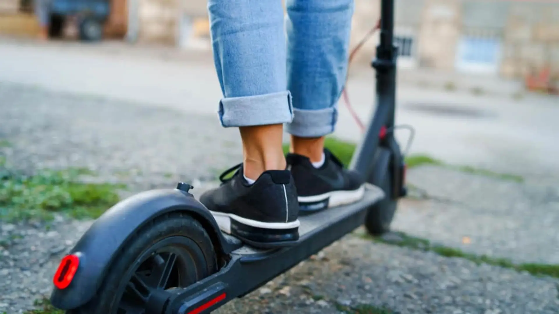 Primer plano de pies de mujer en zapatillas conduciendo patinete eléctrico por carril bici.