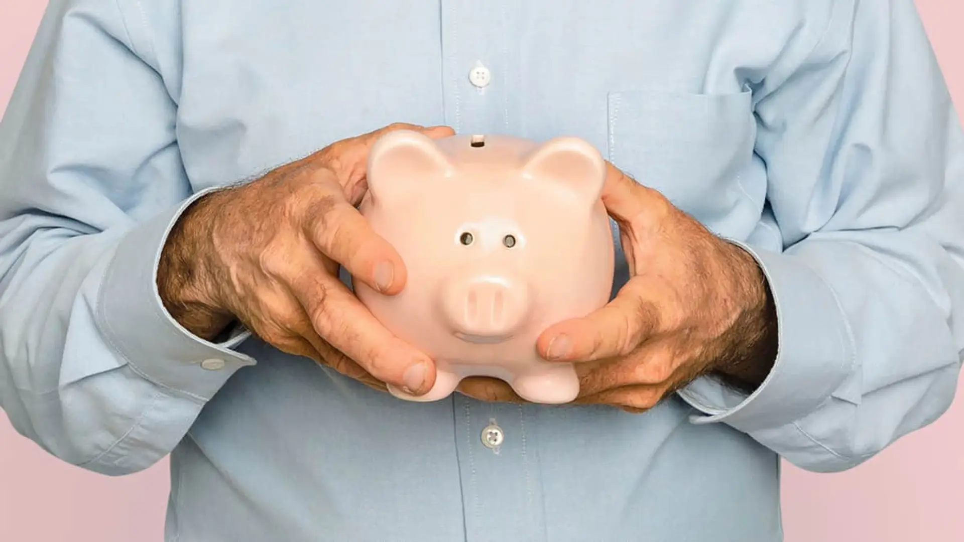 País Vasco tiene el triple de dinero en pensiones privadas que el resto de España: el atractivo de las EPSV Manos de un hombre mayor sosteniendo una hucha de cerdo, símbolo del ahorro para la jubilación y los planes de pensiones.