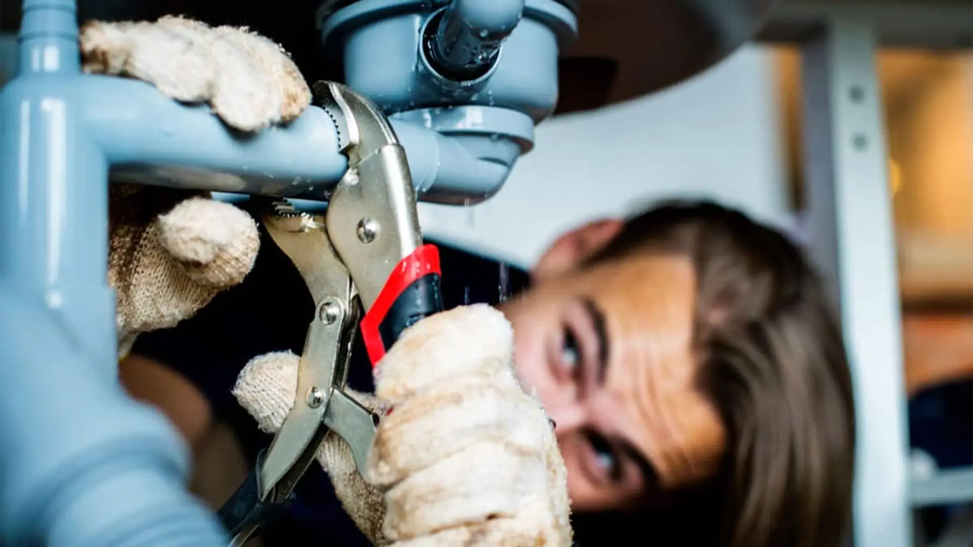 Persona reparando una tubería bajo un fregadero con una llave de presión
