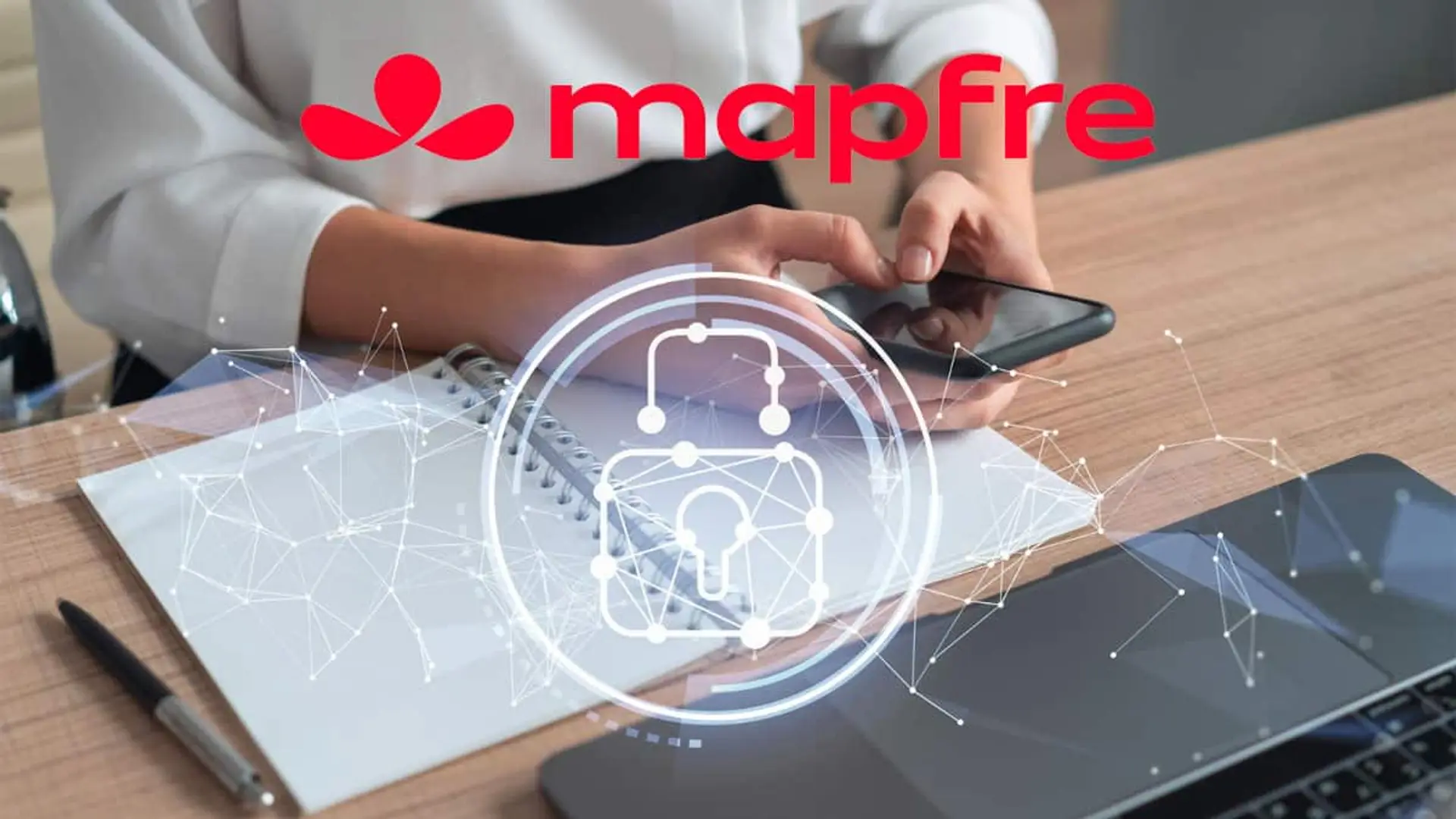 Persona usando un móvil sobre una mesa con un icono de ciberseguridad superpuesto y el logotipo de Mapfre