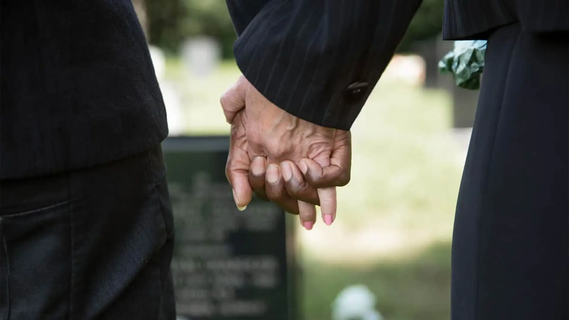 Pagas más por Netflix que por tu seguro de decesos: esto cuesta asegurar un funeral en España Primer plano de dos personas de luto cogidas de la mano en un cementerio, simbolizando el apoyo durante el duelo en un funeral.