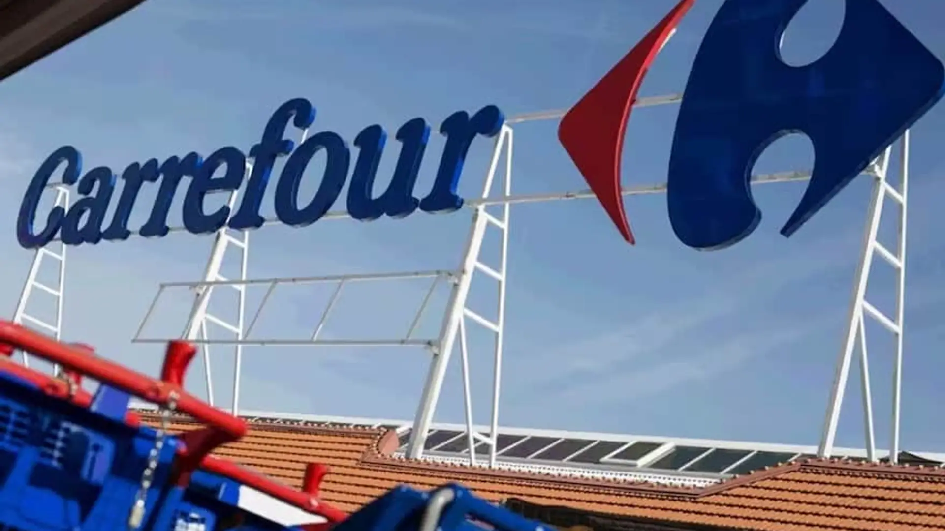 Cartel exterior con el logotipo de supermercados Carrefour y carros de la compra en primer plano.