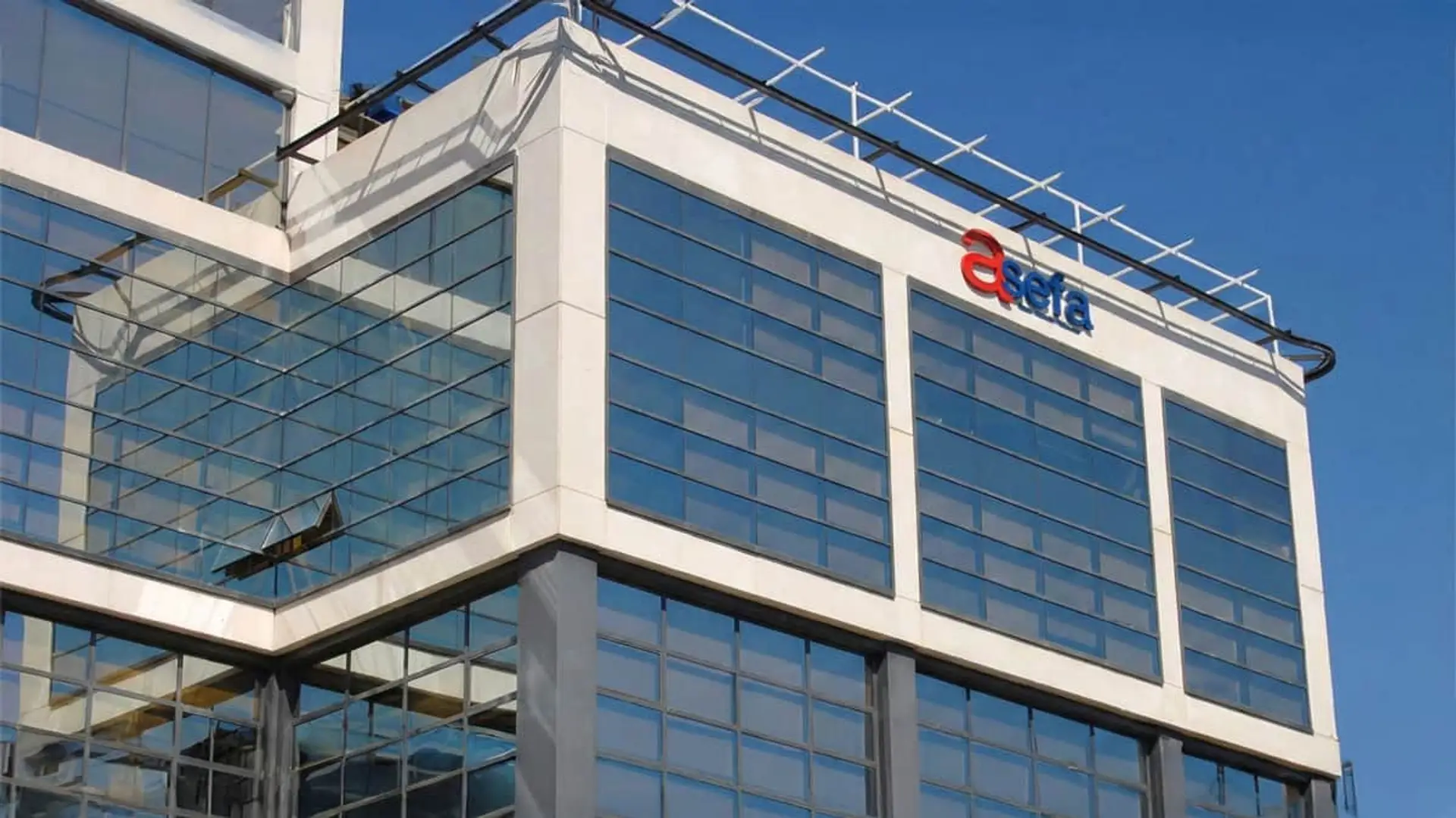 Fachada del edificio de oficinas de Asefa Seguros con ventanales de cristal y cielo azul despejado.