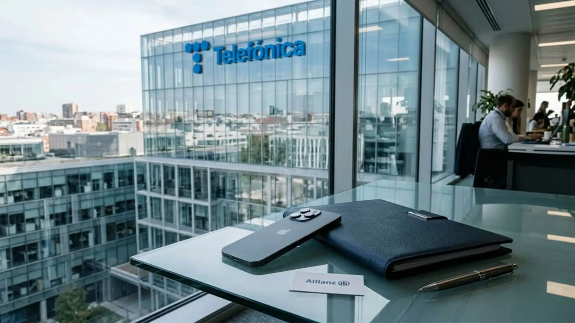 Sede de Telefónica vista desde una oficina con un móvil, una carpeta y una tarjeta de Allianz sobre la mesa.