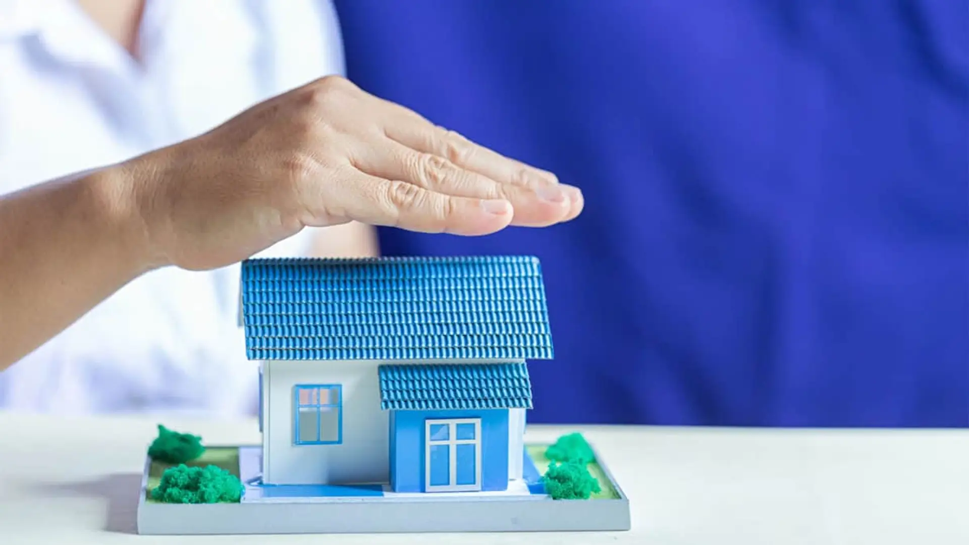 Manos protegiendo maqueta de casa familiar simbolizando la cobertura del seguro de hogar.