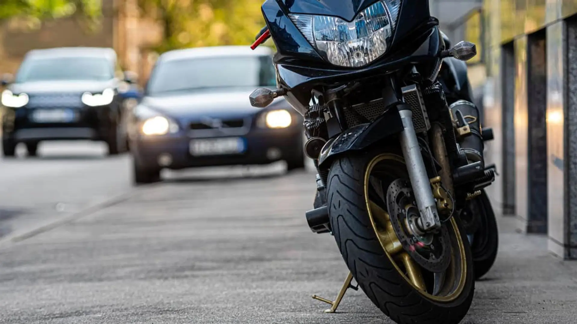 Los seguros de coche y moto se encarecen, pero hogar, salud y decesos bajan en marzo Motocicleta estacionada en la acera con coches circulando al fondo para representar seguros de motos y autos.