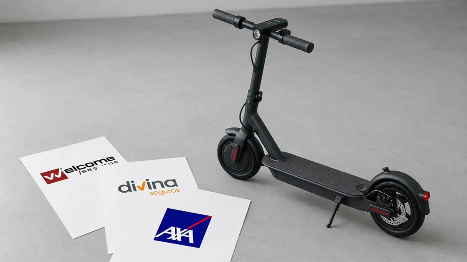 El seguro básico de patinete cuesta de media 81 euros, pero la compañía más barata no es la misma en cada modalidad Patinete eléctrico urbano junto a folletos de seguros Welcome, Divina y AXA sobre fondo gris, movilidad protegida.